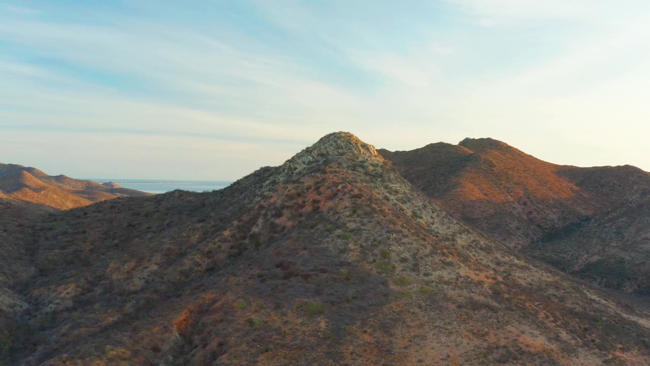 Cabo Pulmo rocky peak seen from above with distant flat land and a faint coastal horizon visible at left, warm hillside light, and no visible people.