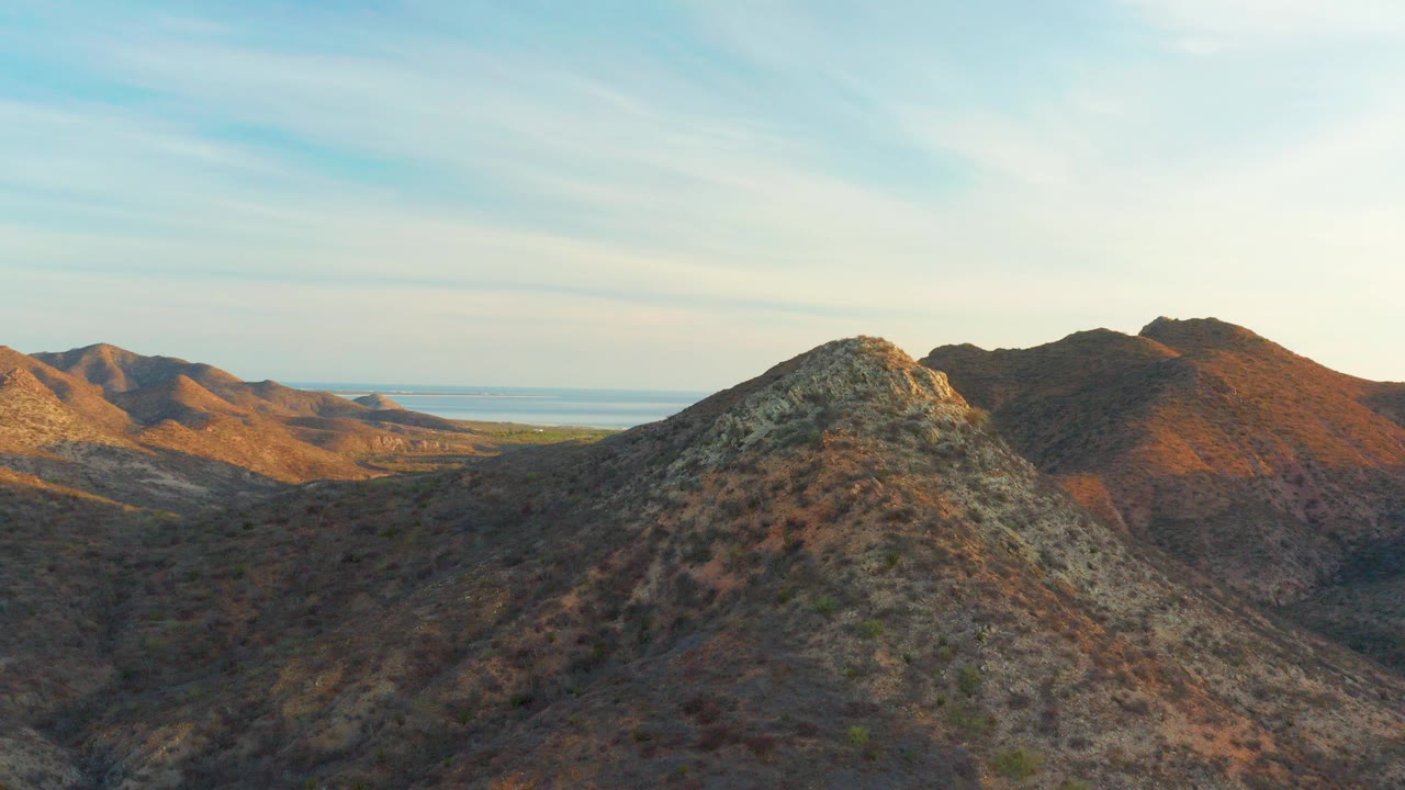 Rocky desert hills with distant water under a pale sky.