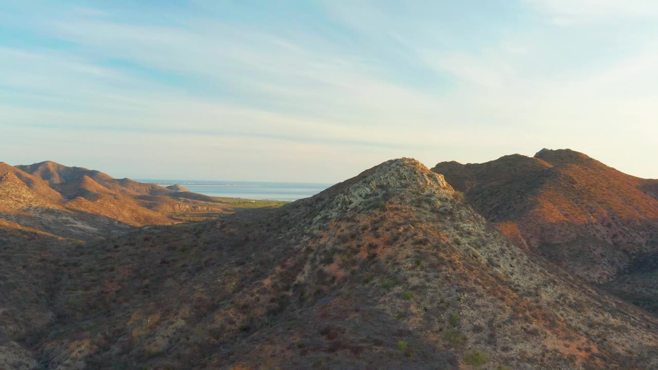 A rocky foreground ridge sits near the center of the Cabo Pulmo aerial view, with brown hills behind it, distant water at left, and no visible people.