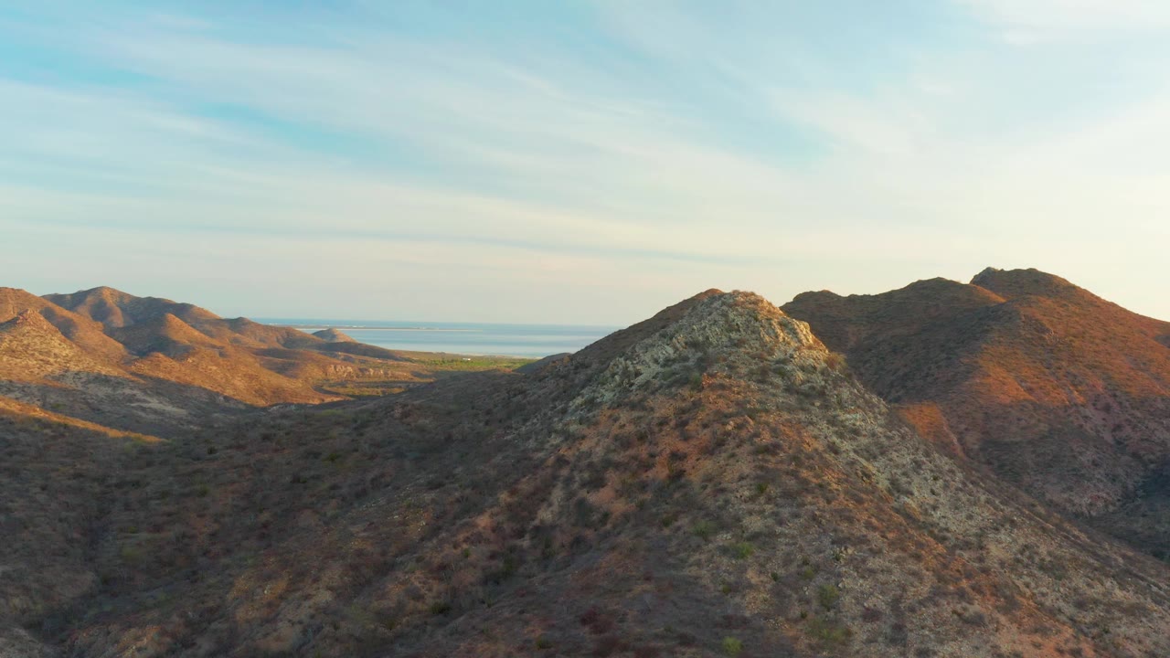 Sunlit ridges and darker shadowed slopes spread across the Cabo Pulmo desert mountain range, with a thin band of water in the distance and no visible people.