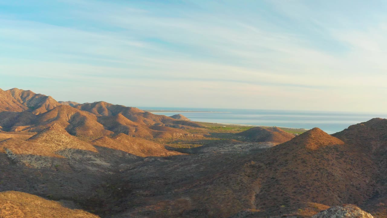 Aerial landscape of arid hills, open valley, and ocean beyond.