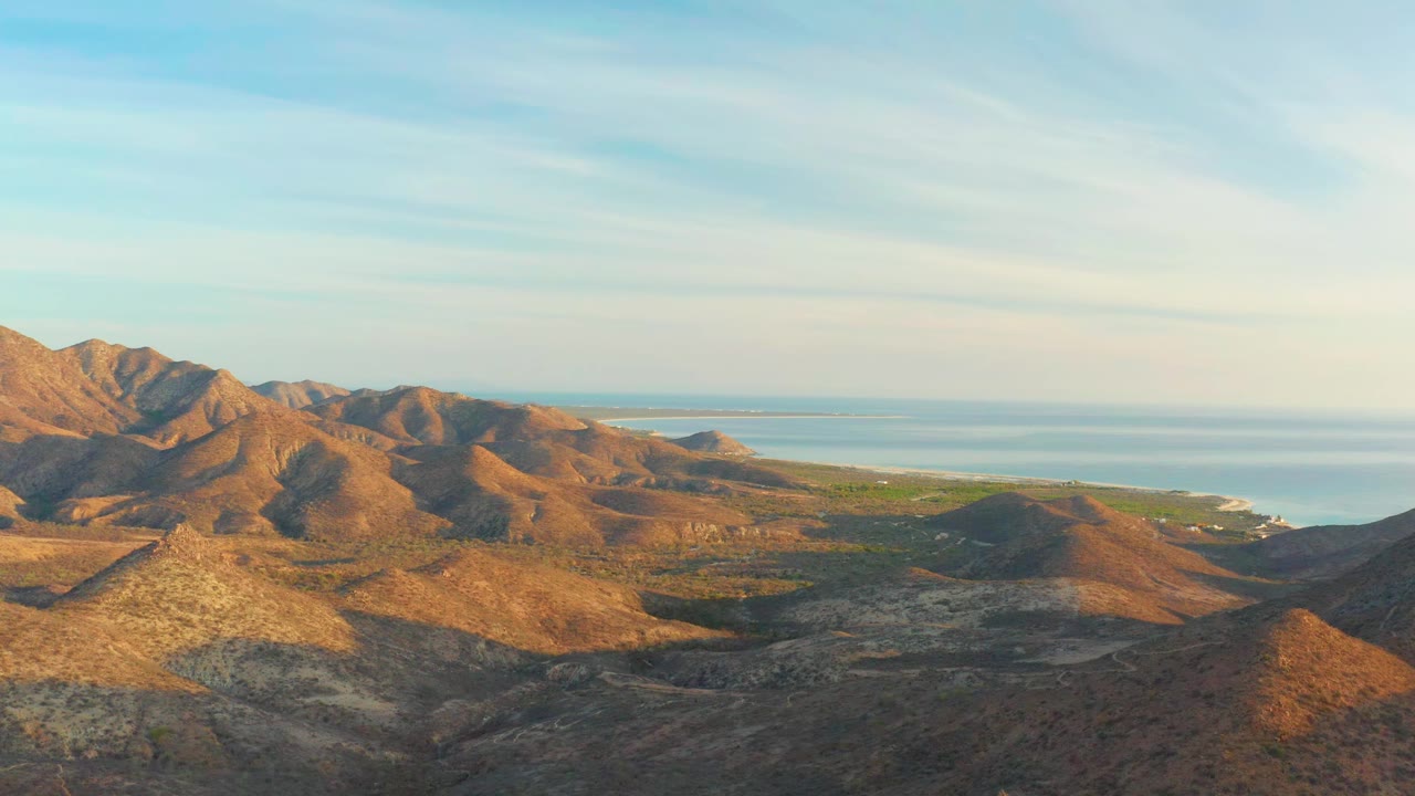Cabo Pulmo mountain ridges stretch across the foreground and midground, with a brighter strip of coastline and ocean under a clear sky, and no visible people.