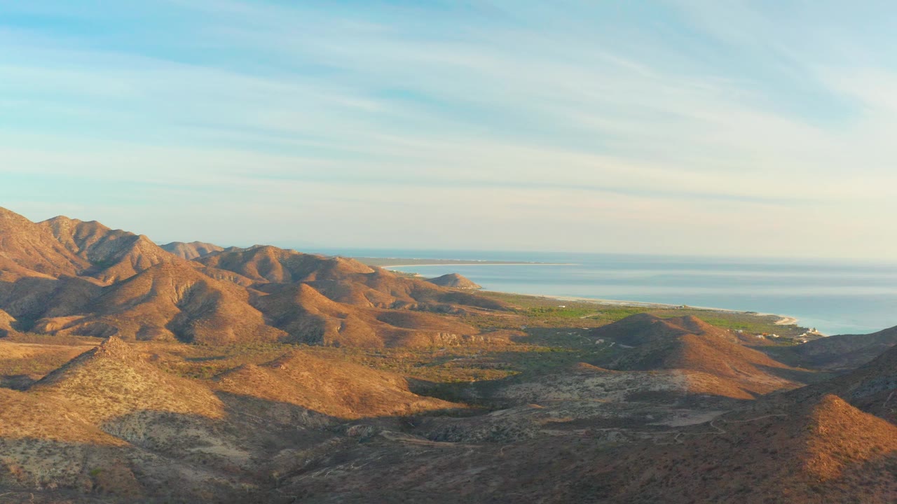 A high view across Cabo Pulmo arid hills shows blue water behind the terrain, with warm highlights on the slopes and no visible people.