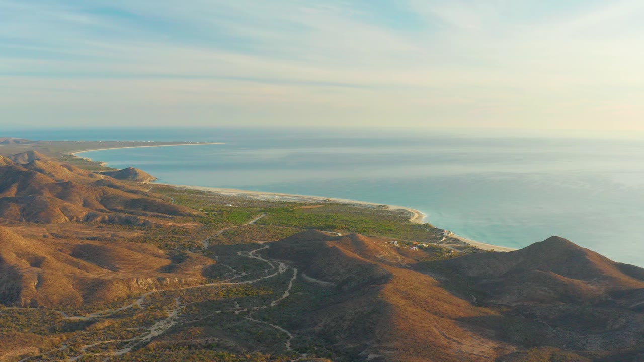 Aerial view of brown hills, winding road, green coastal plain, and blue ocean.