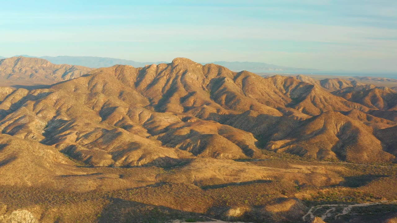Wide aerial landscape of desert hills and distant mountains.