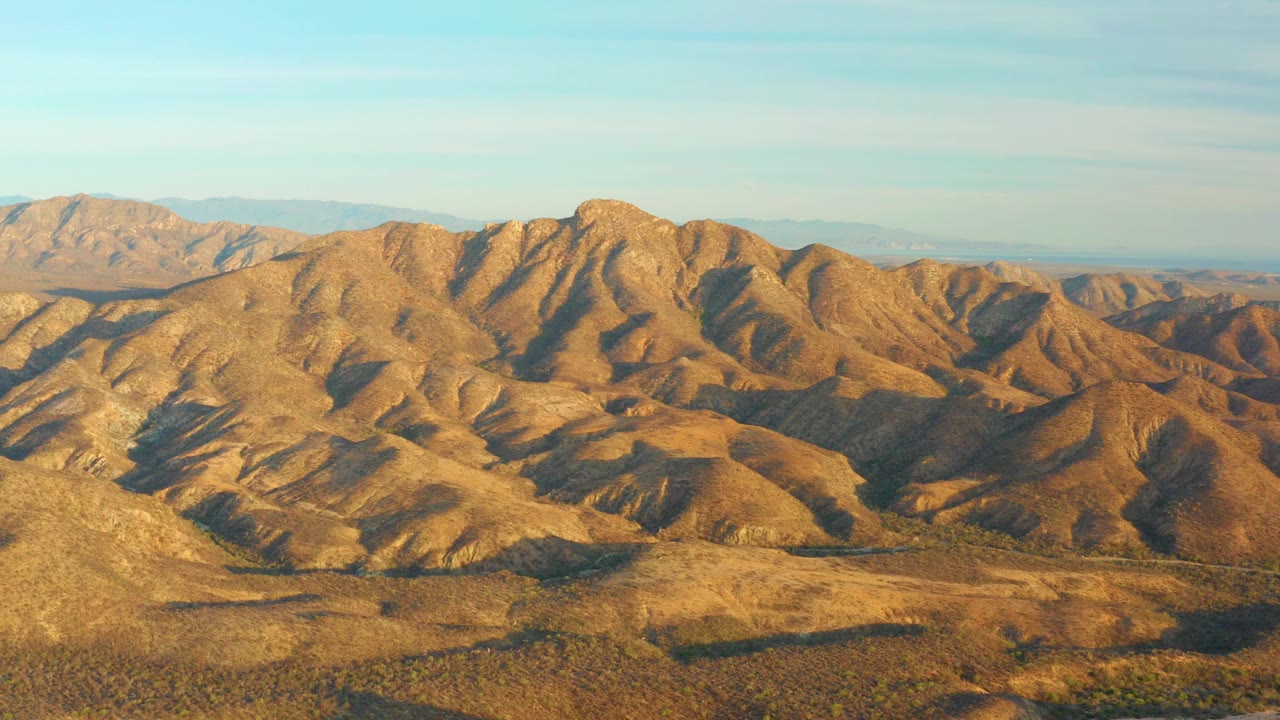Opening frame of rolling brown hills near Cabo Pulmo, Baja California Sur, with scrubby foreground desert, distant ridges, warm light, and no visible people.
