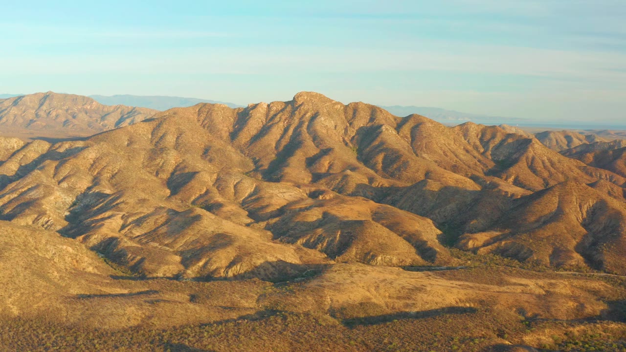 Cabo Pulmo arid hills continue across the frame, with dark gullies cutting through sunlit slopes and no visible people.
