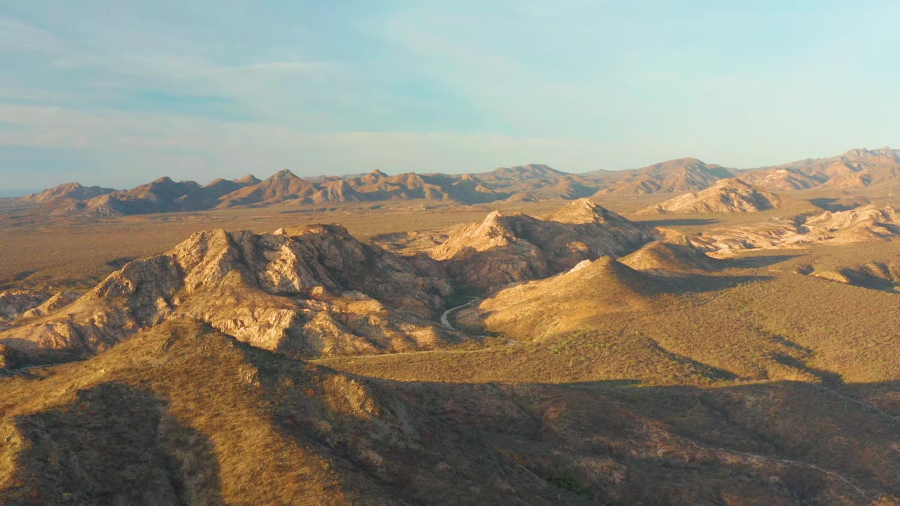 Cabo Pulmo desert terrain seen from above, with a dark shadow stretching across the foreground ridge, sunlit tan hills beyond it, and no visible people.