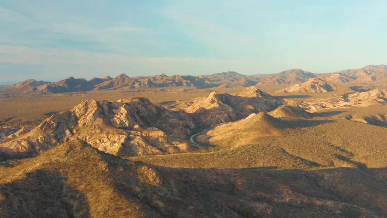 Cabo Pulmo aerial desert landscape with the foreground darkened by shadow, midground ridges catching low warm light, distant mountains, and no visible people.