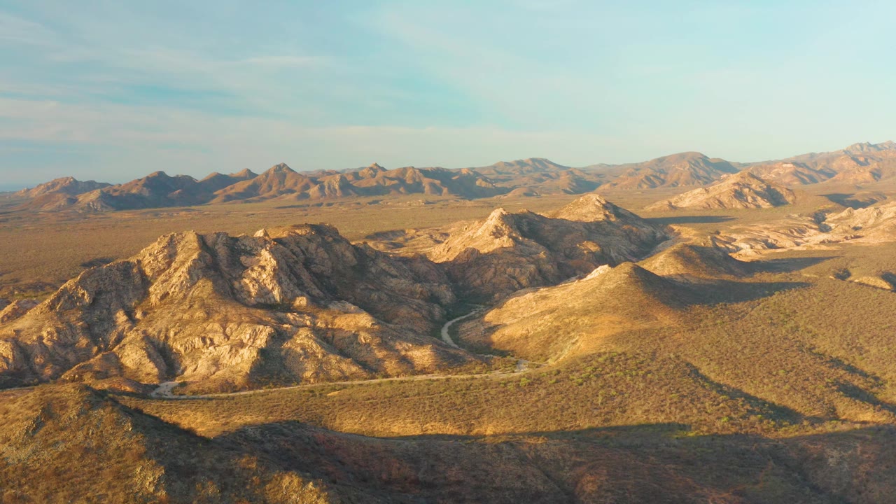 At three seconds, Cabo Pulmo's arid hills remain centered, with the winding road tracing the valley, golden light on the rock faces, darker shaded ground in the foreground, and no visible people.