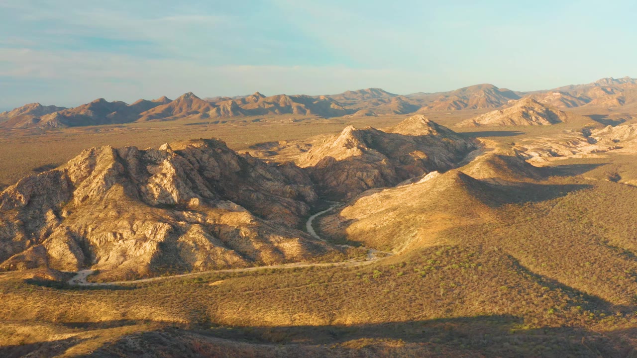 The Cabo Pulmo aerial frame holds on tan ridges and scrubland as the road bends through the center, with no visible people.