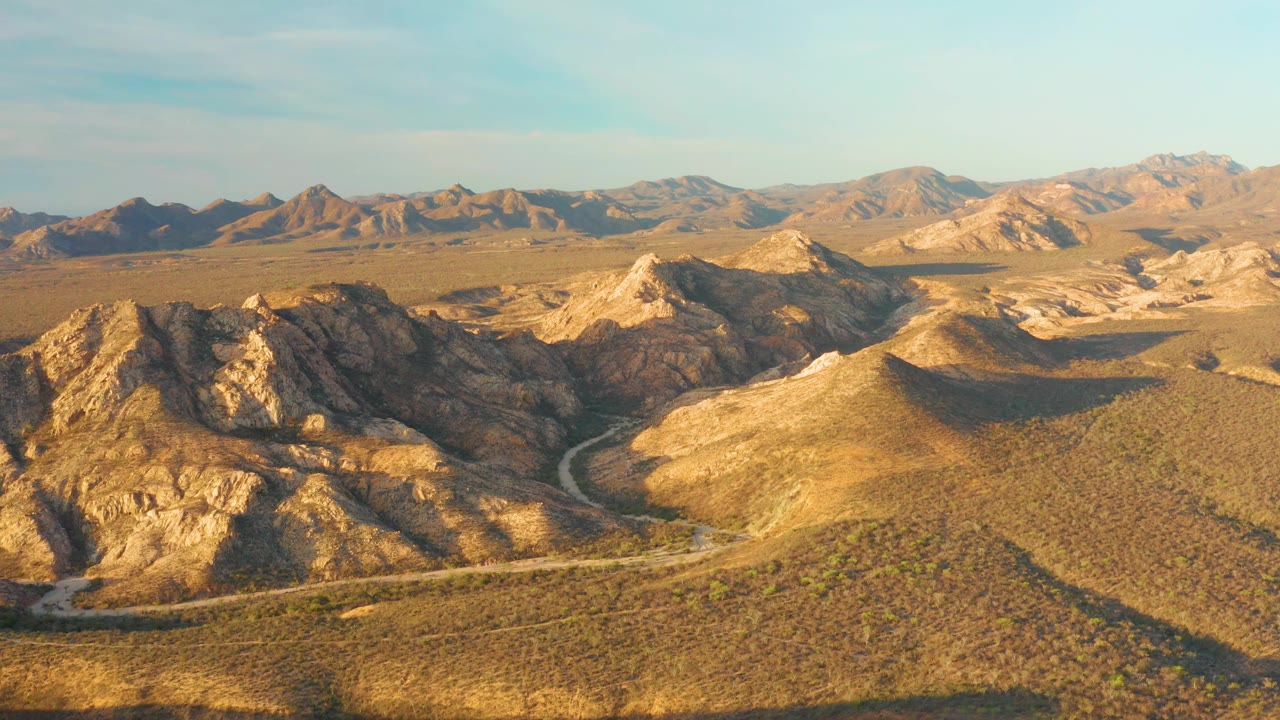 Sunlit rocky hills and a curving road in dry open terrain.