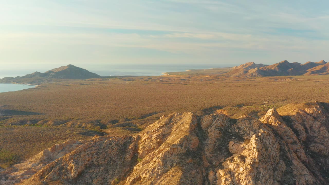 Wide coastal desert landscape with rocky ridge and distant sea