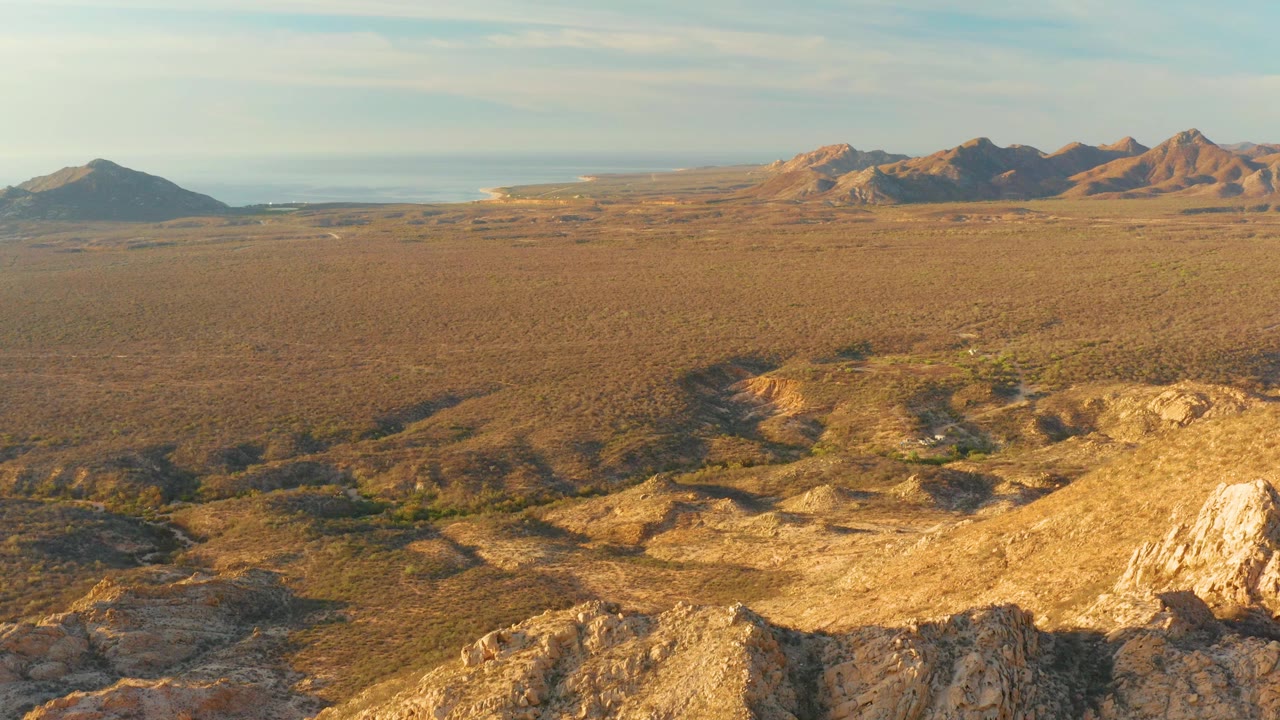 A wide Cabo Pulmo landscape frame shows pale foreground rock, brown scrubland, distant hill ridges, clear sky, and no visible people.