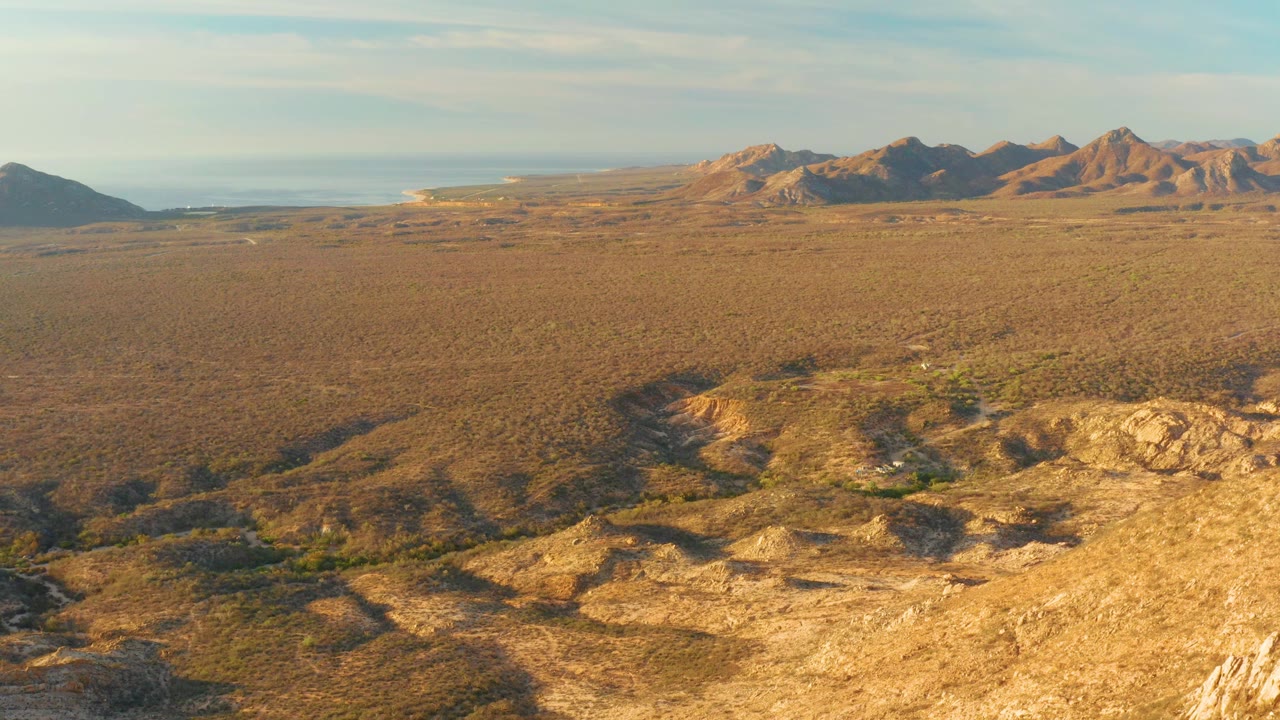 Desert aerial with mountains under a pale partly cloudy sky