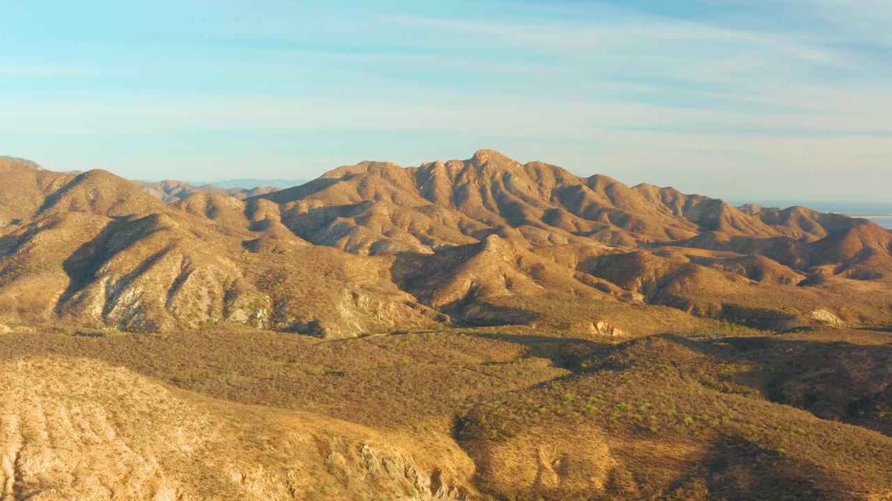 Layered brown desert hills lead toward rocky mountains in Cabo Pulmo, Baja California Sur, Mexico, with warm light on the ridges and no visible people.