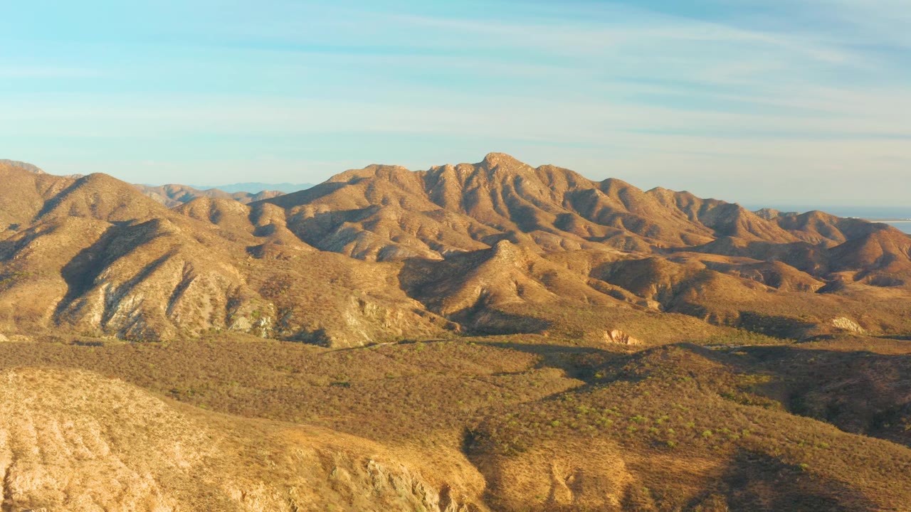 A large rocky desert slope enters the left side of the Cabo Pulmo mountain panorama, with dry low hills stretching across the center and no visible people.