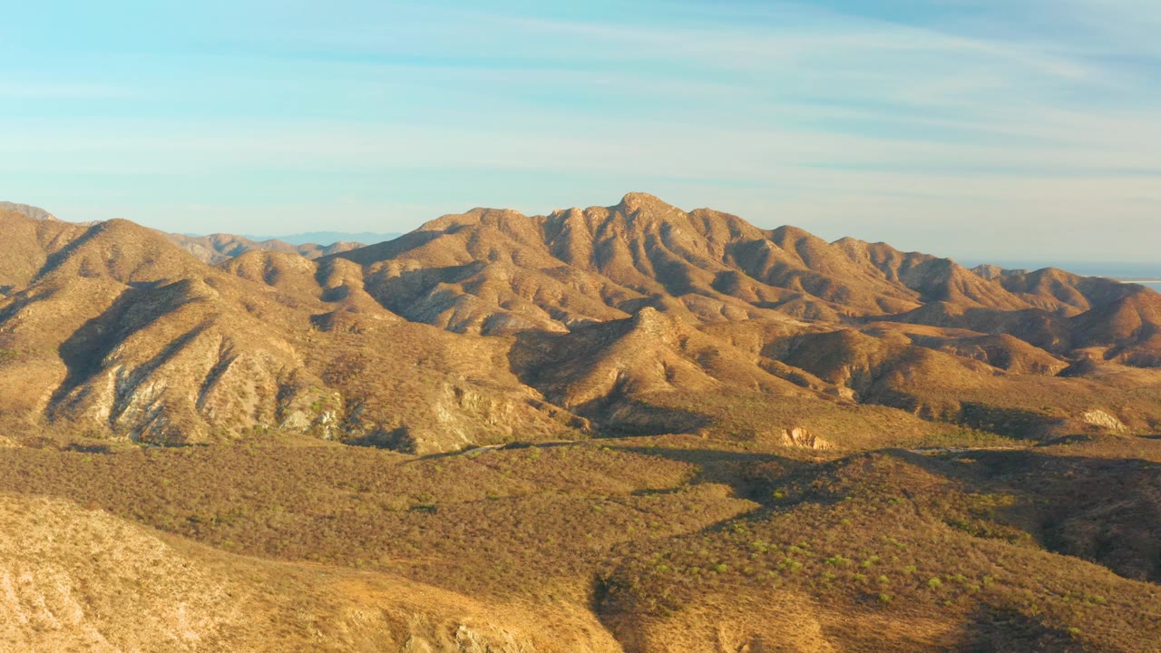 At 0:02, layered arid hills in Cabo Pulmo stretch toward a rocky mountain line, with long shadows crossing the valley floor and no visible people.