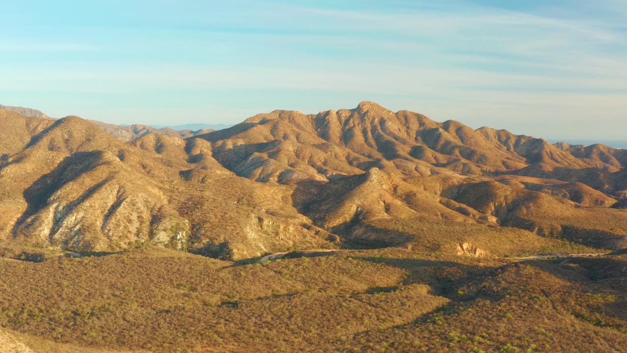 Opening frame over Cabo Pulmo, Baja California Sur, with rocky brown mountains, scrubby valley floor, a faint road in the lower terrain, and no visible people.