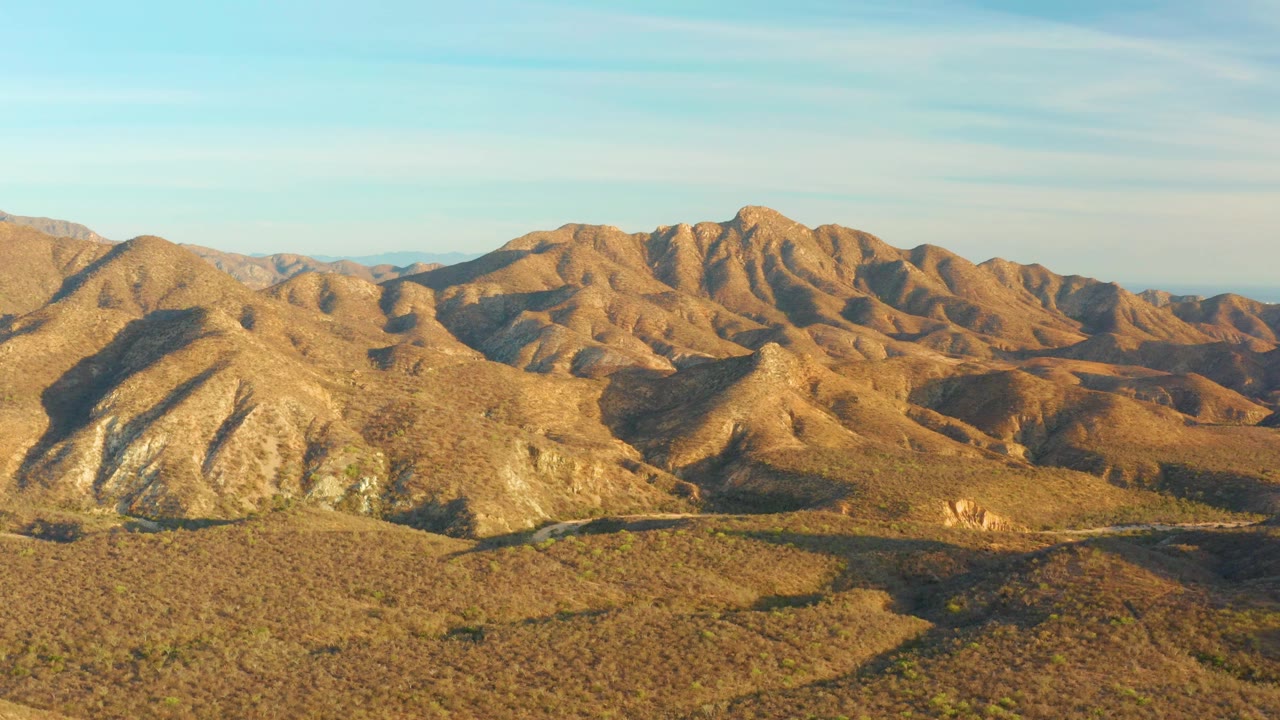 Sunlit desert mountains with scrubland and a road cutting through the valley.