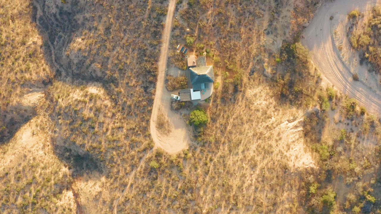 Small house and dirt tracks seen from above in dry rural terrain.