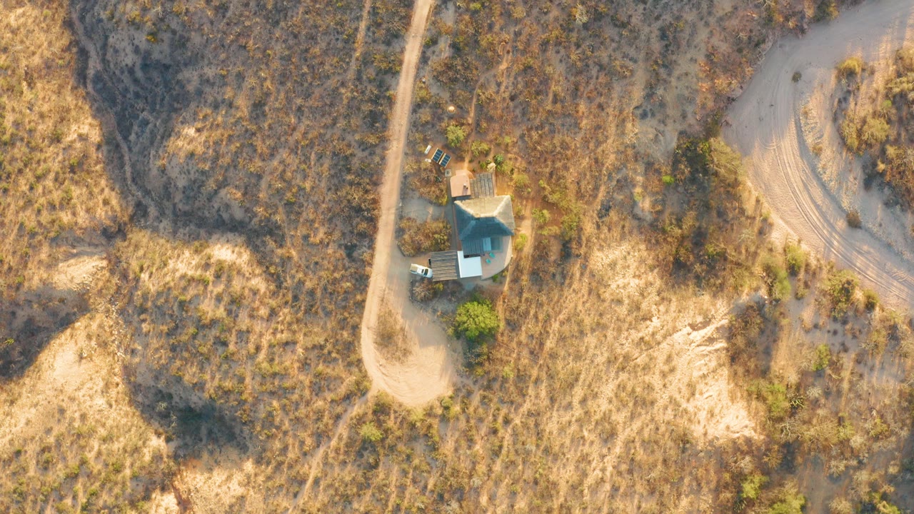 Cabo Pulmo aerial view with the roofed house surrounded by dry brush, a straight dirt track on one side, a curving road on the other, and no visible people.