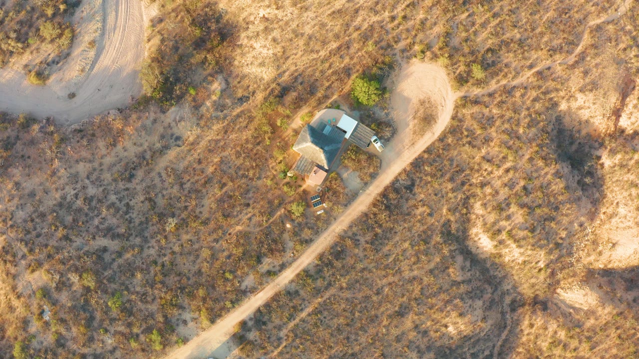 Aerial view in Cabo Pulmo showing the small roofed structure beside a curved dirt track, with open dry vegetation spreading across the frame and no visible people.