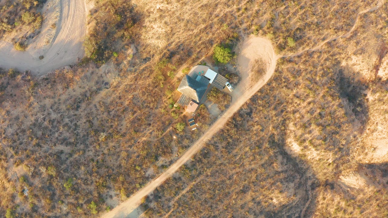 Curved road and small building surrounded by dry brush and grass.