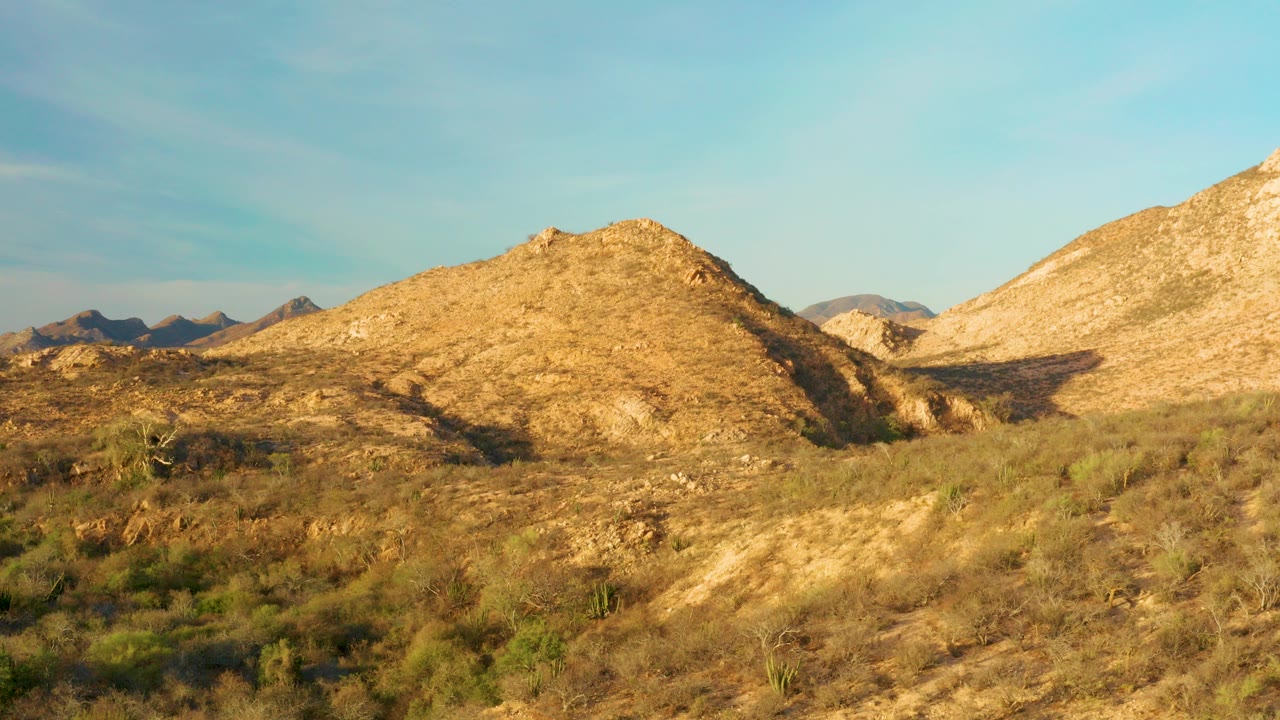 Cabo Pulmo desert hills fill the frame with tan scrub, distant rocky ridges, warm sunlight, and no visible people.