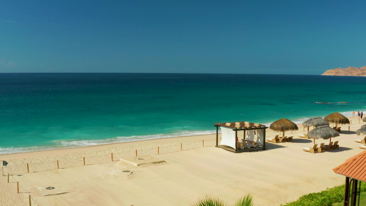 Wide resort beach view with surf, umbrellas, and a canopy structure.