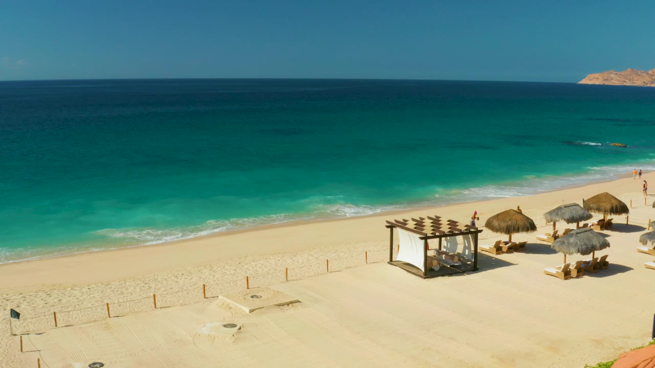 Turquoise surf and sandy beach with thatched umbrellas and lounge chairs at the lower right.