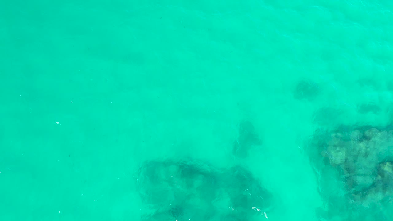 At Hilton Los Cabos in Mexico, soft ripples pass over darker underwater rock shapes near the lower center and upper right, with no visible people.