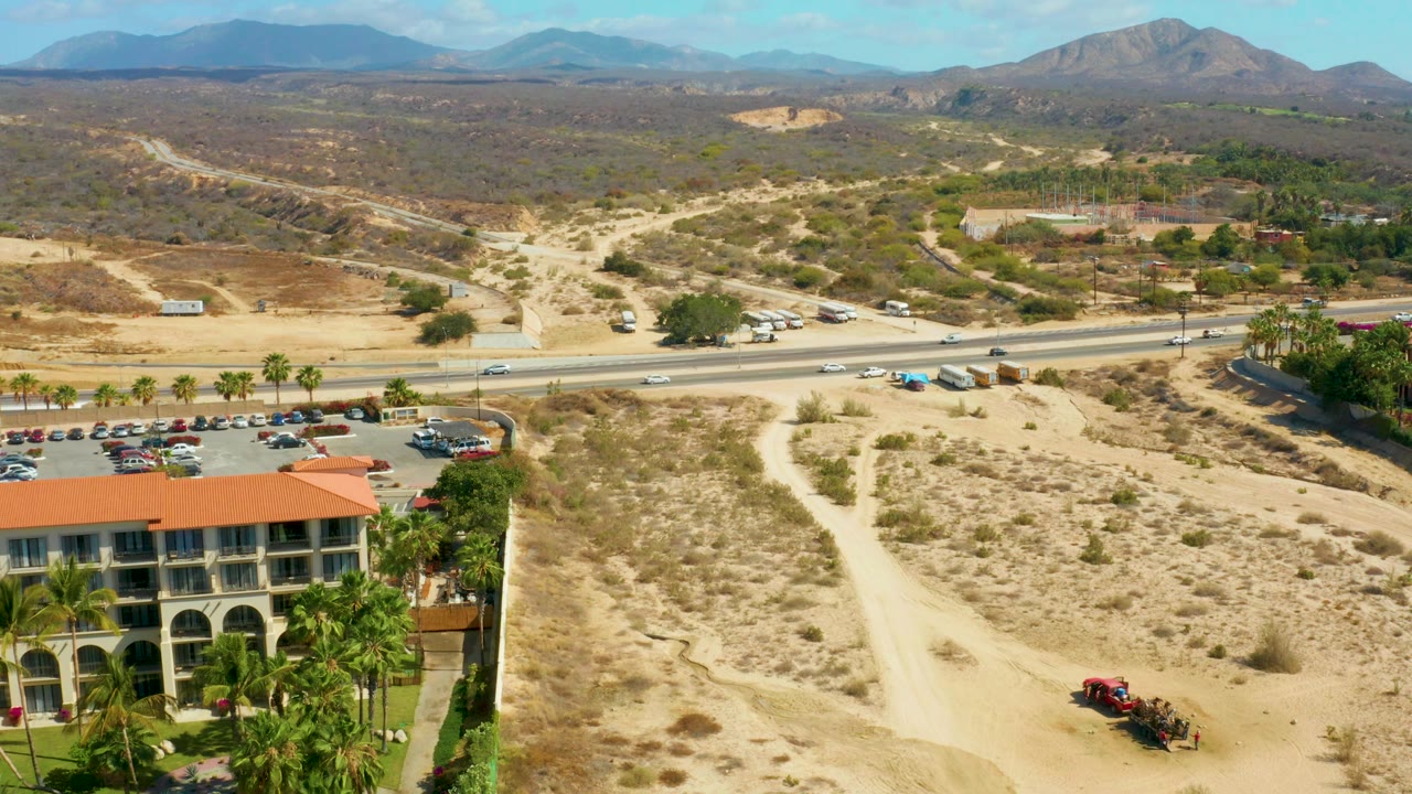 Wide aerial view over hotel roof, parking lot, highway, desert trails, and mountains.