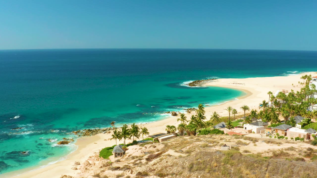 Curving white beach bordered by turquoise water and palm trees.