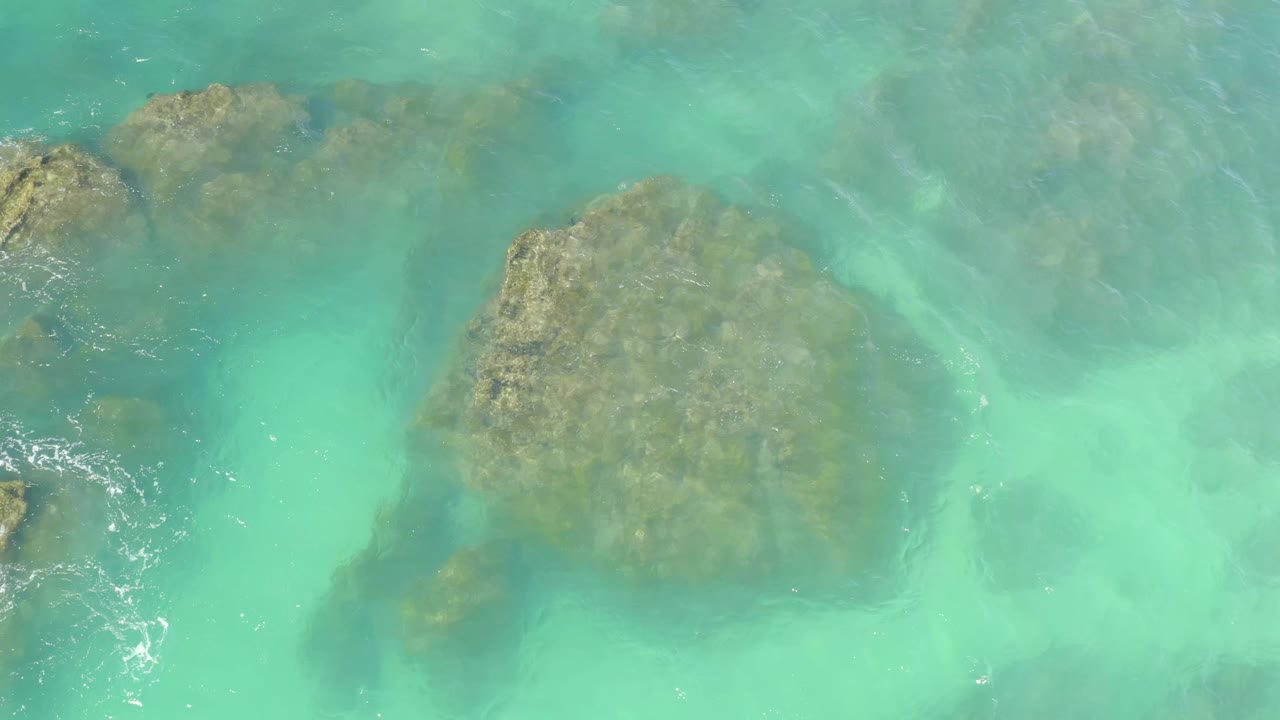 Clear blue-green water ripples over submerged rocks at Hilton Los Cabos, Mexico, with the main rock still centered and no visible people.