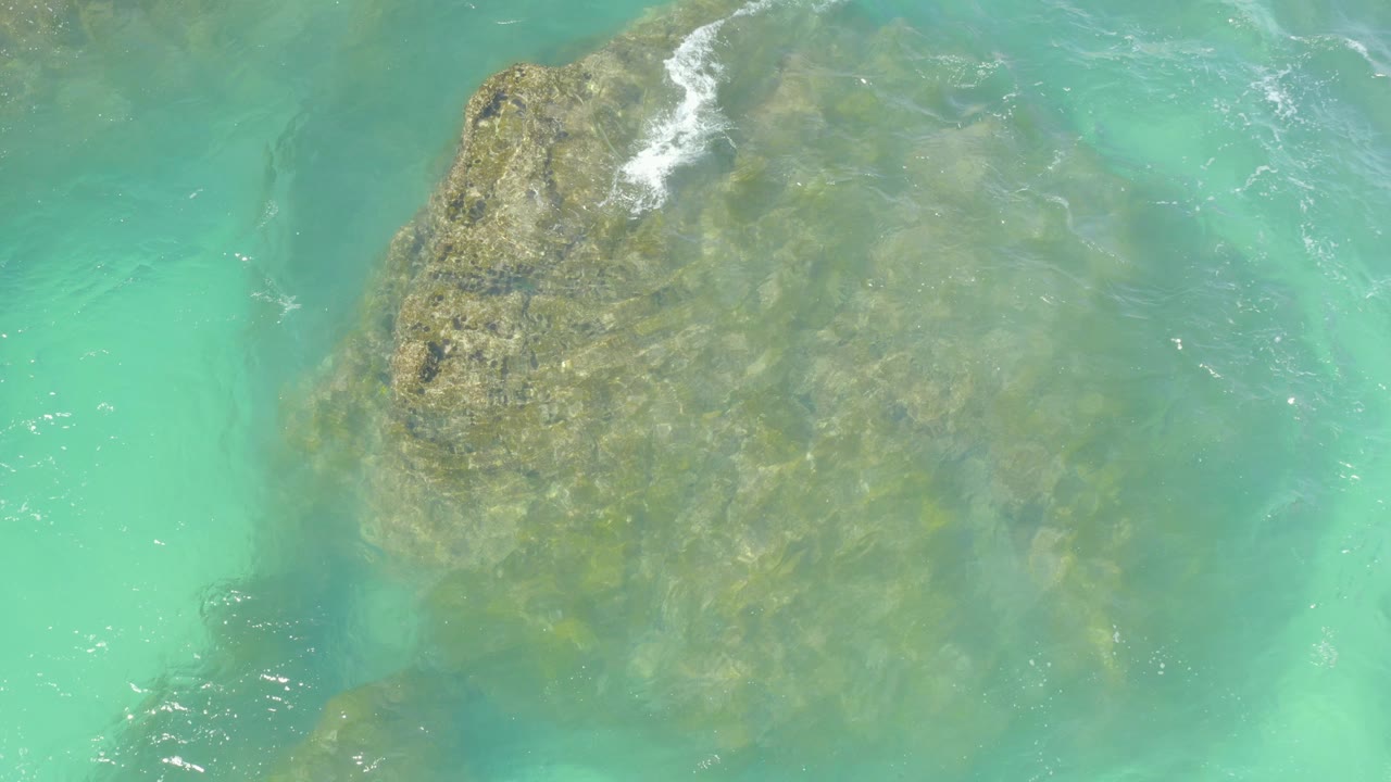 Submerged rock under turquoise water with foam at the upper edge.