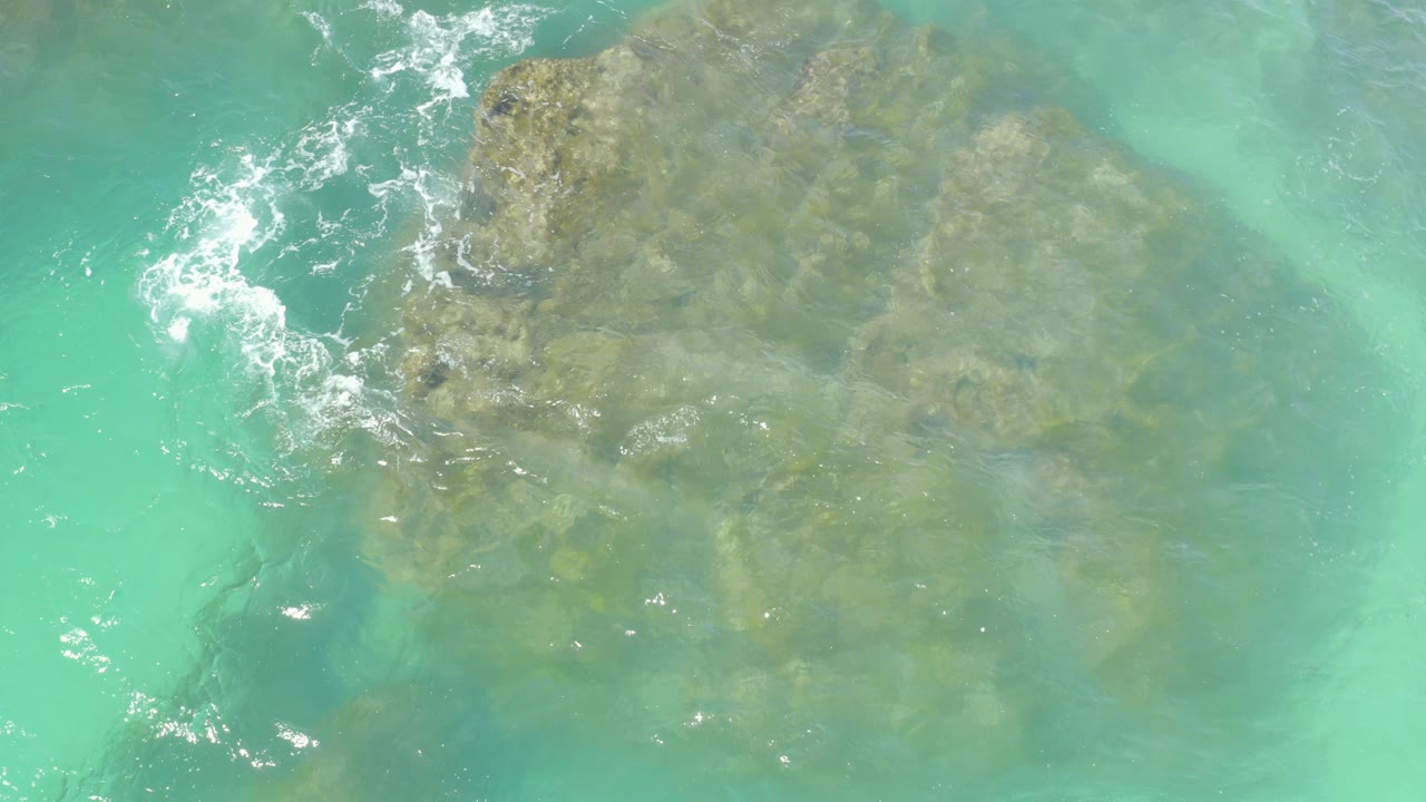 Top-down view of turquoise water at Hilton Los Cabos, Mexico, showing submerged rocks under light ripples with no visible people.