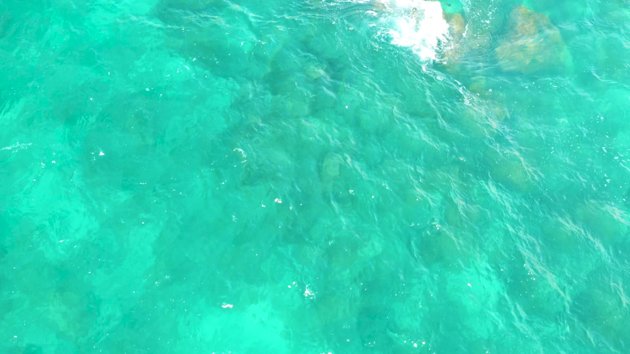 Hilton Los Cabos, Mexico overhead water frame with turquoise ripples, faint rock forms under the surface, and no visible people or shoreline.