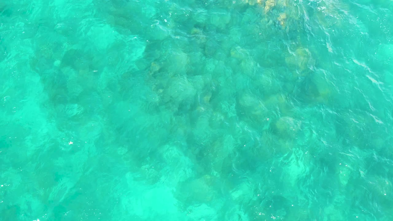 Clear blue-green water reveals a mottled rocky seabed at Hilton Los Cabos, Mexico, with light streaks crossing the surface and no visible people.