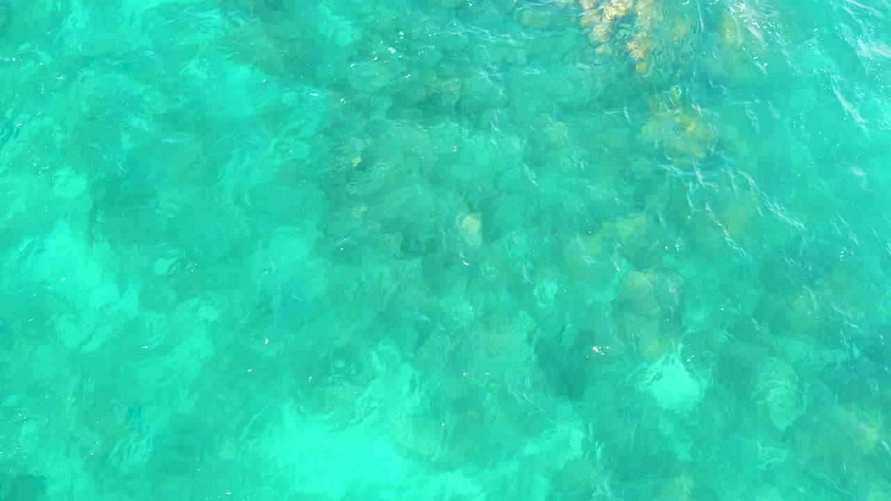 Turquoise ocean water sits over darker rock patches and pale sandy gaps at Hilton Los Cabos, Mexico, with no visible people.
