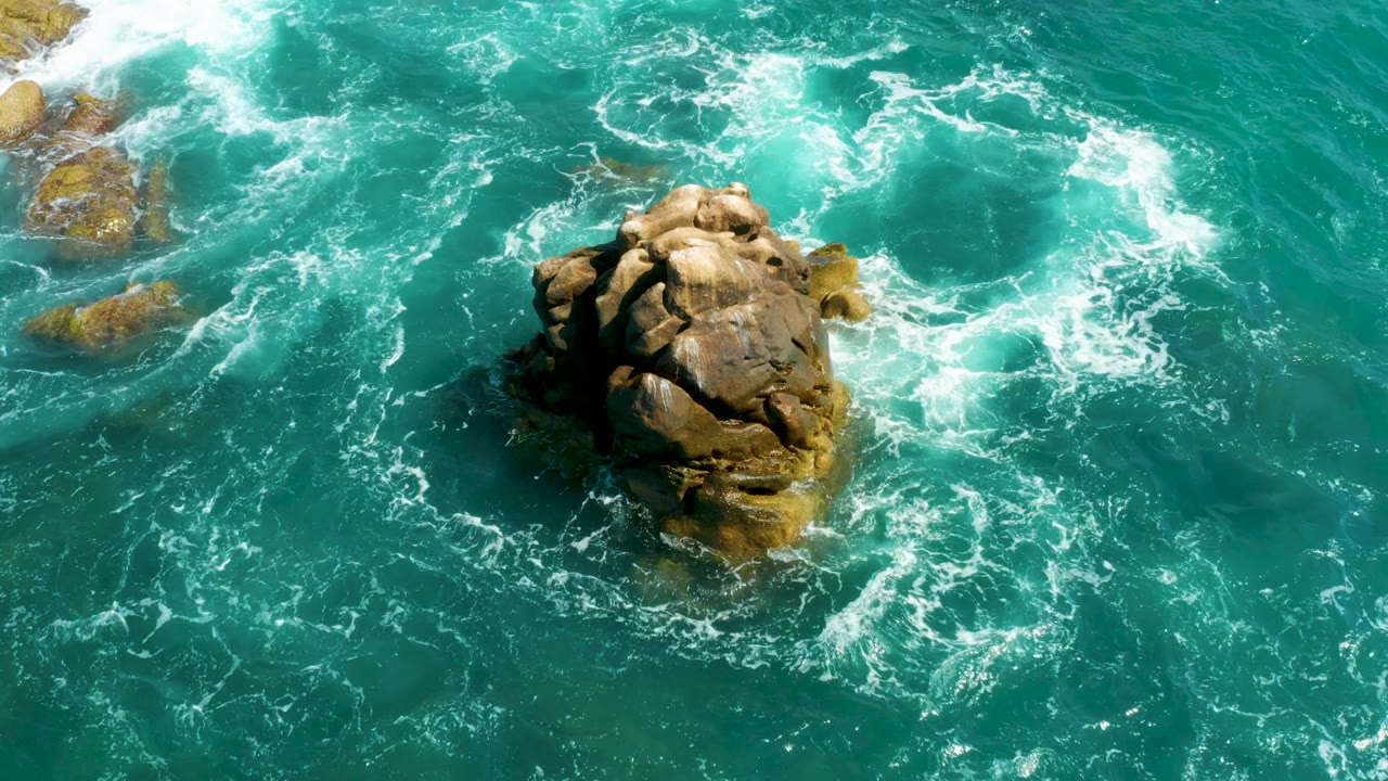 Rocky formation with surf curling across turquoise ocean water.