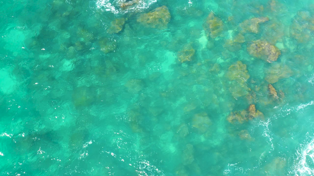 Top-down view of turquoise water at Hilton Los Cabos, Mexico, with submerged rocks near the upper half and no visible people.