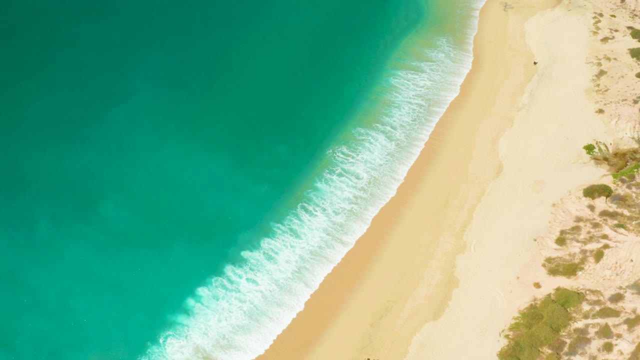 Overhead turquoise water meeting a pale sandy beach.
