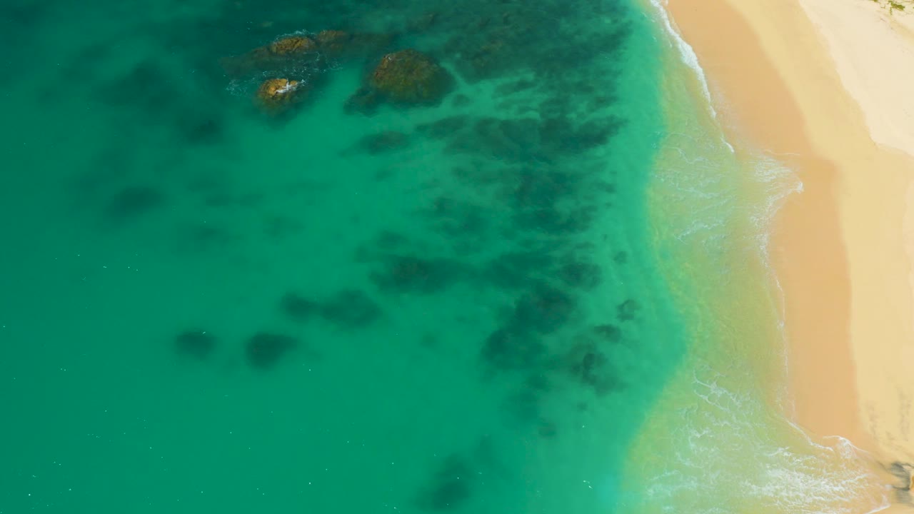 Beach shoreline with teal water and darker underwater patches.