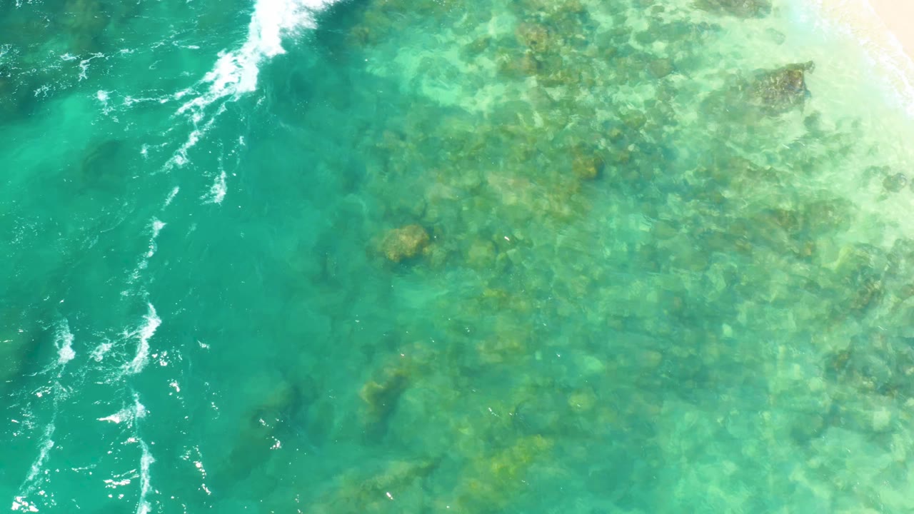 Clear green-blue water with submerged rocks and thin white foam streaks.