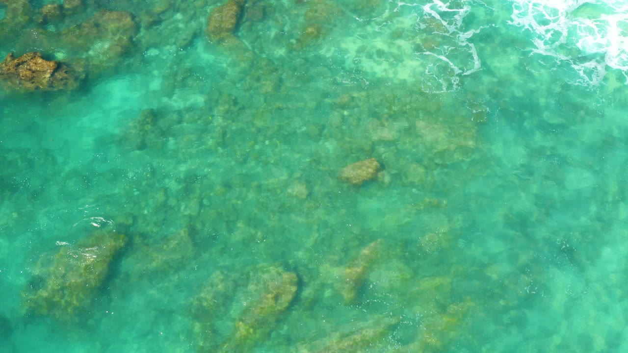 Submerged rocks sit under turquoise water with a small foam patch at the top.