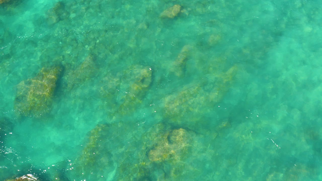 Top-down view of clear turquoise water over scattered submerged rocks at Hilton Los Cabos, Mexico, with no visible people.