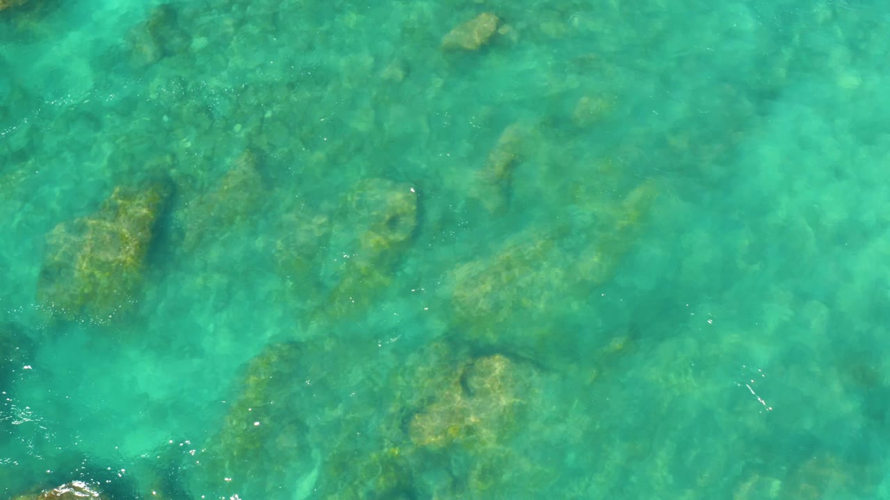 Clear ocean water reveals darker rocks and marine growth beneath small surface ripples at Hilton Los Cabos, Mexico, with no visible people.