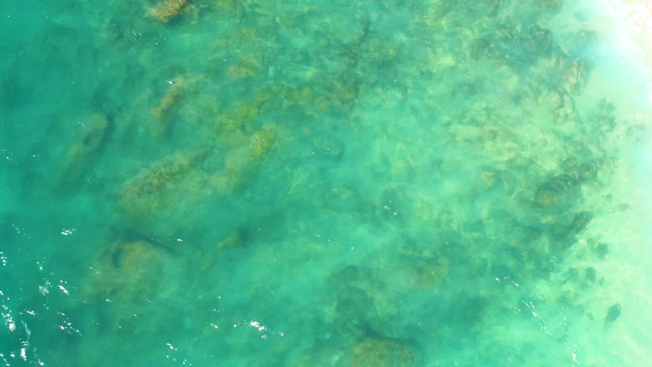 Turquoise ocean water over submerged rocks and pale surf edge