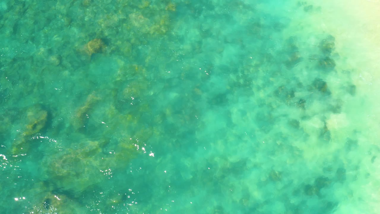 Clear water at Hilton Los Cabos reveals darker submerged rocks on the left and paler sandy water on the right, with no visible people.